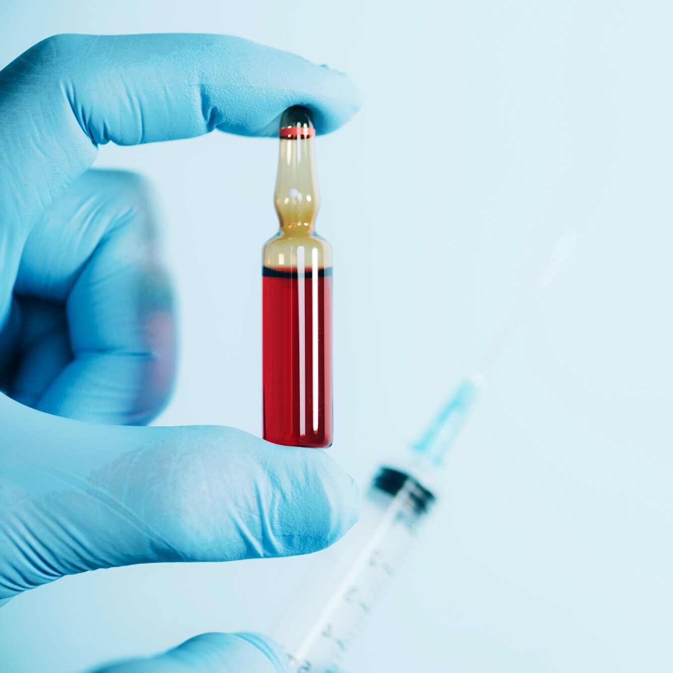 Hands in medical gloves holding syringe and ampoule on blue background. Copy space. Medicine